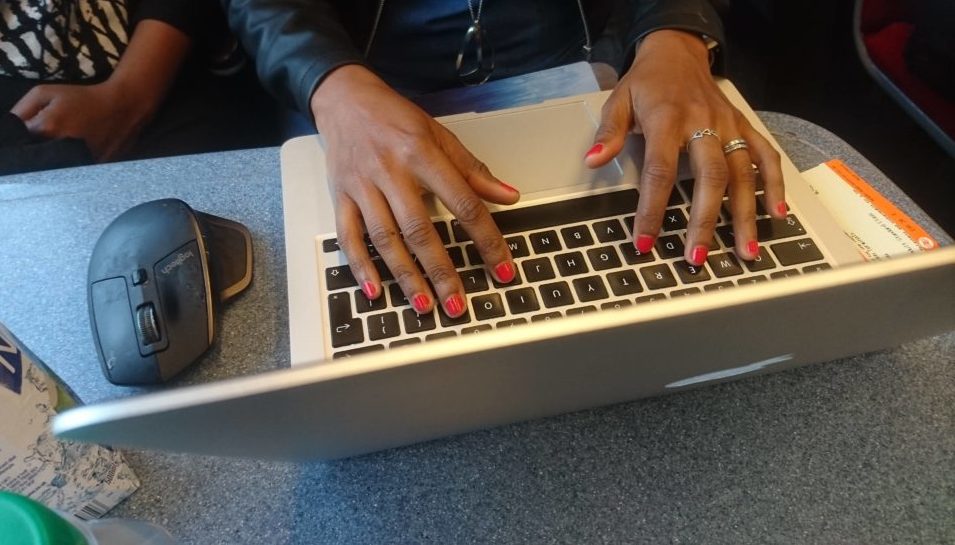 A ladies hands type on a laptop while on the train