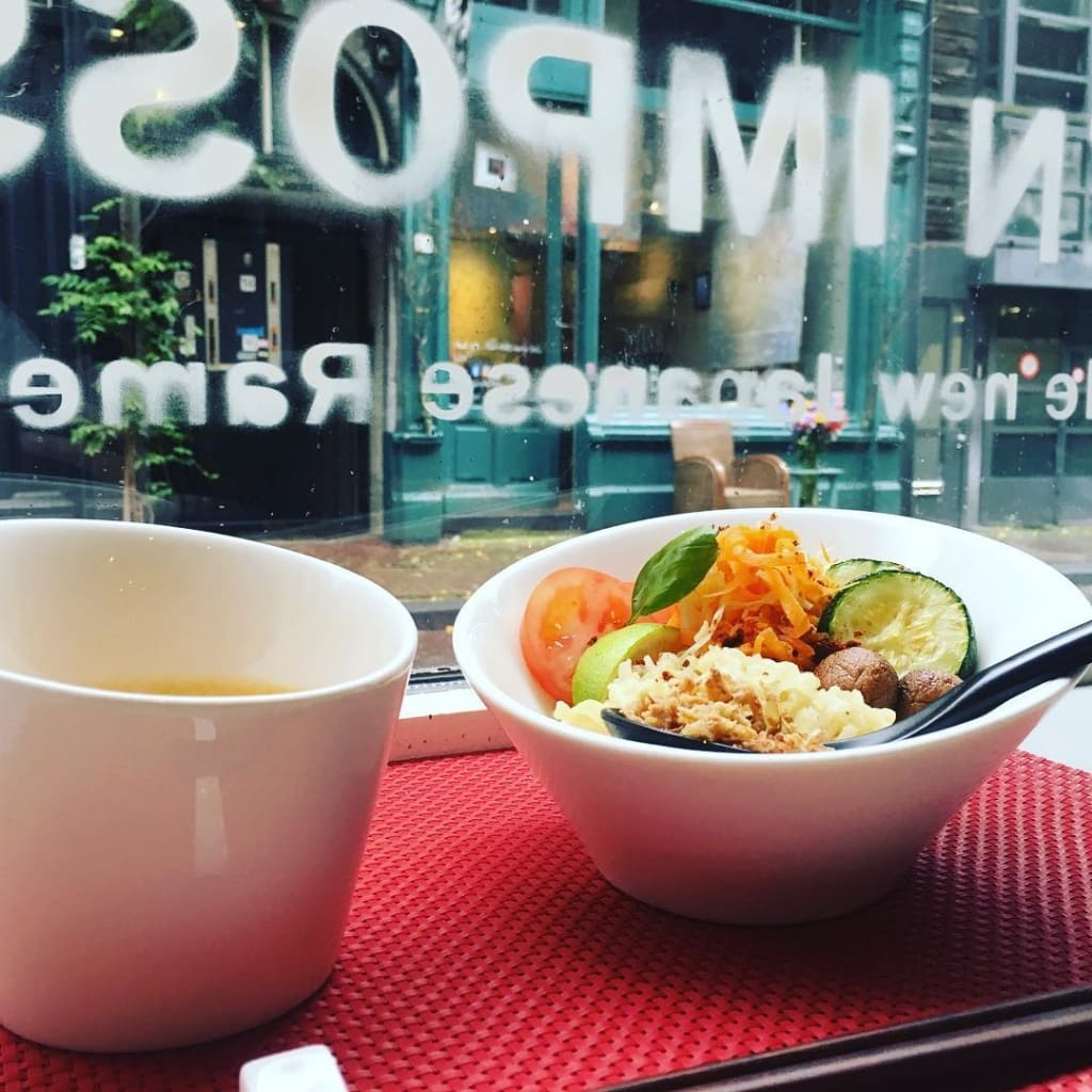 A bowl of Ramen on bench next to the front window of the Men Impossible Restaurant