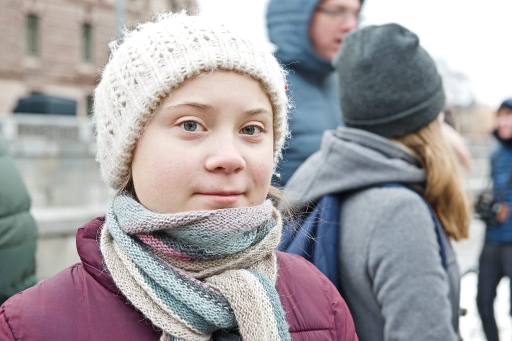 Image of Greta Thunberg, wearing a white wooly hat and looking directly at the camera