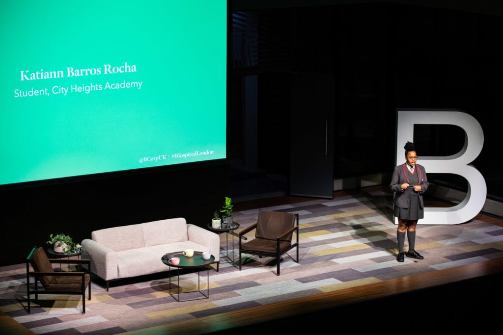 A girl in school uniform stands on stage to deliver her poem