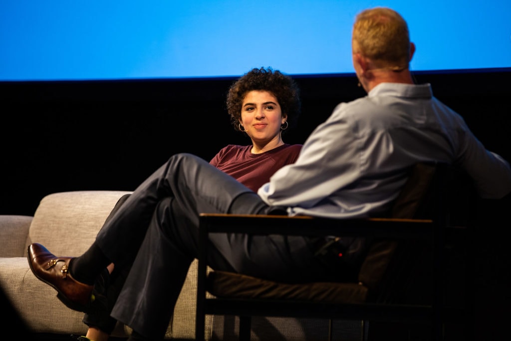 Andrew Medhurst and Noga Levy-Rapoport sit facing each other, in conversation on the stage