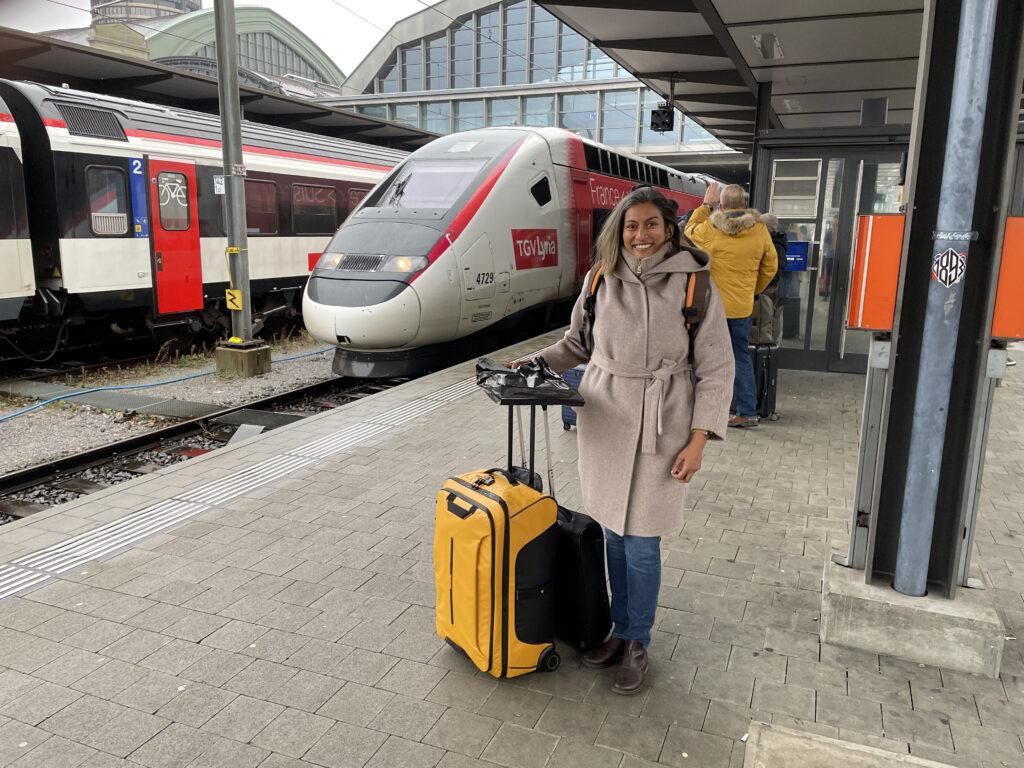 Vineeta on the platform with suitcases with a white and red TGV train behind her